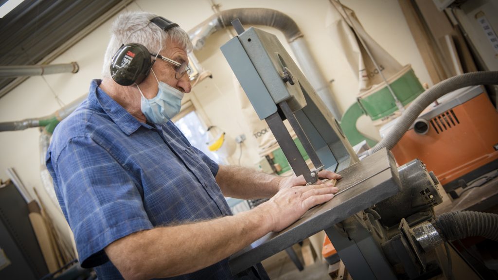 Hobby shop attendee cutting wood at a band saw.