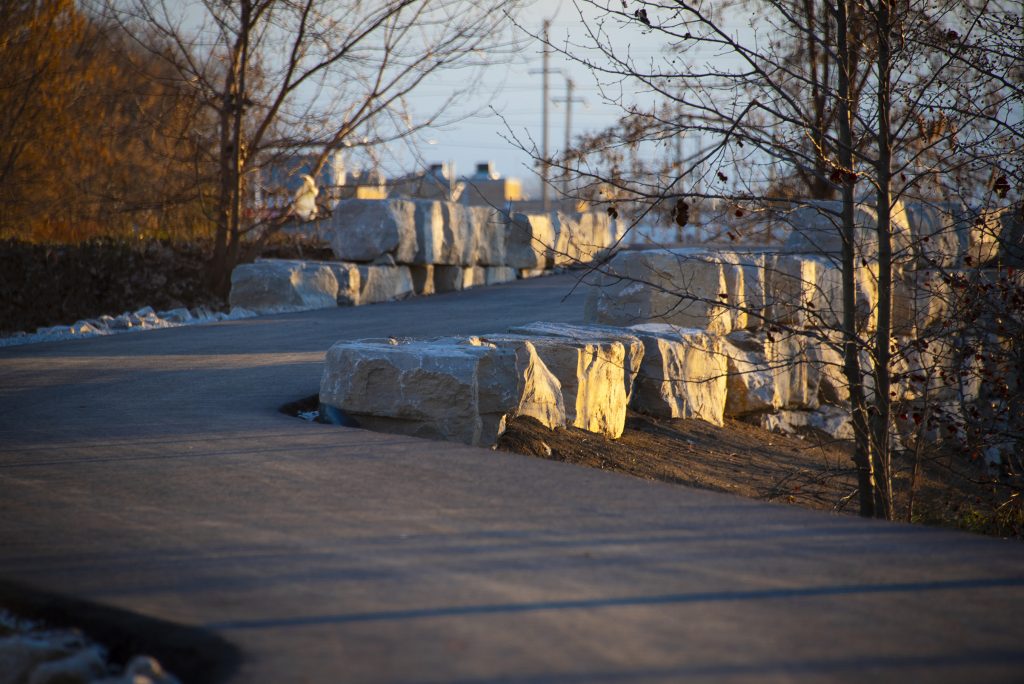 A paved trail running past a stone retaining wall.