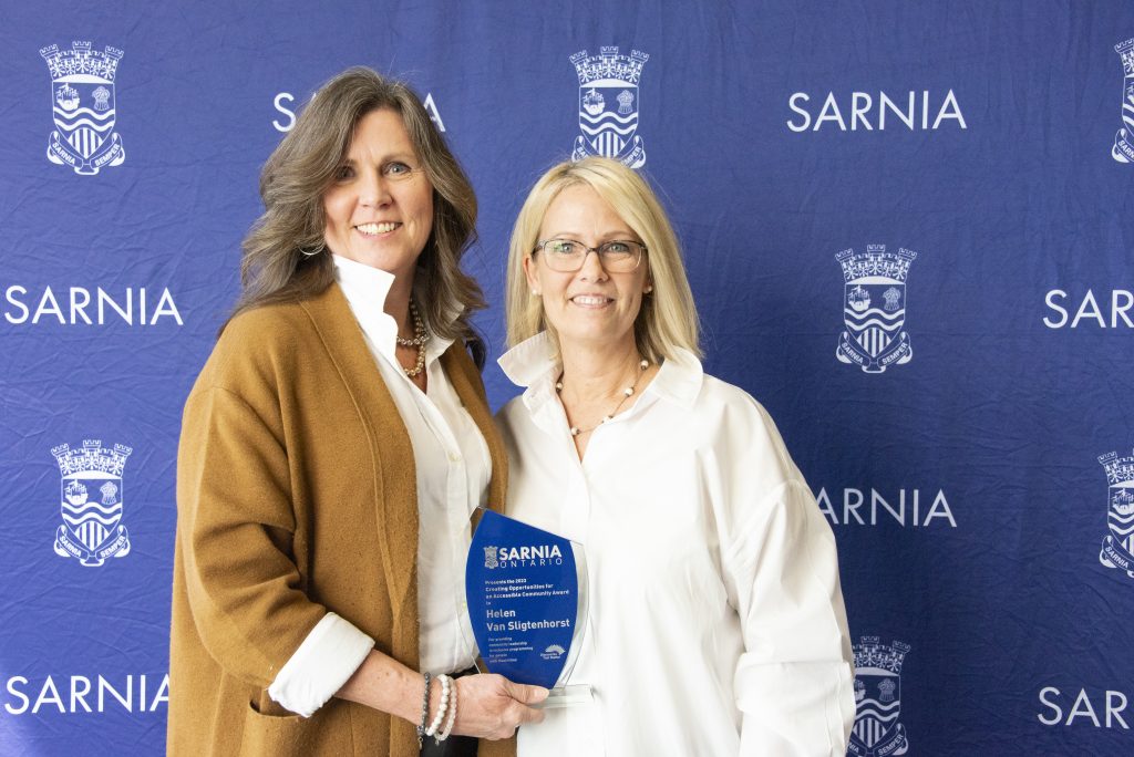 Two individuals smiling, one holding an award.