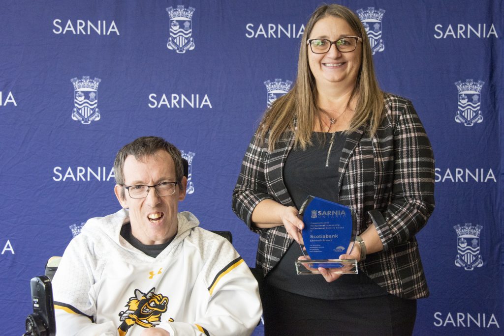 Two individuals smiling, one holding an award.