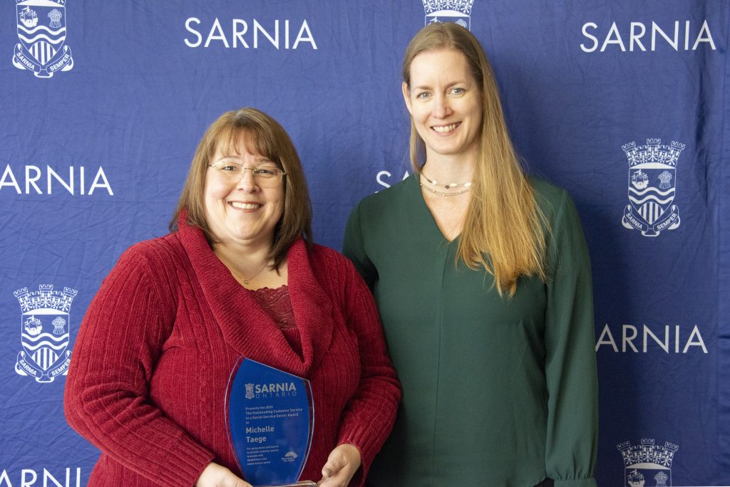 Two individuals smiling, one holding an award.