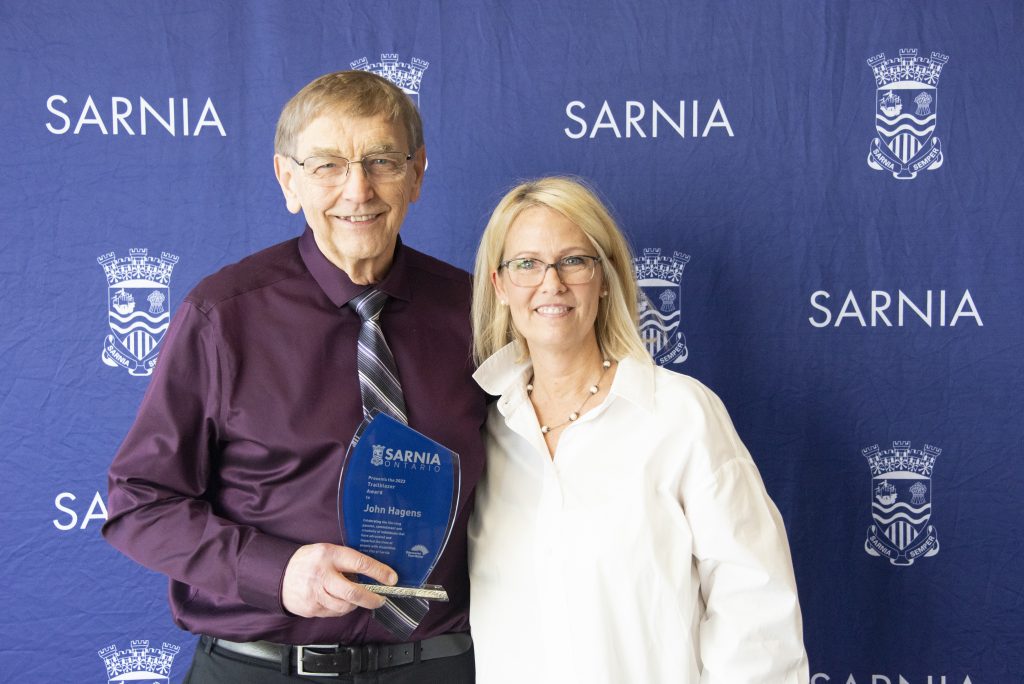 Two individuals smiling, one holding an award.